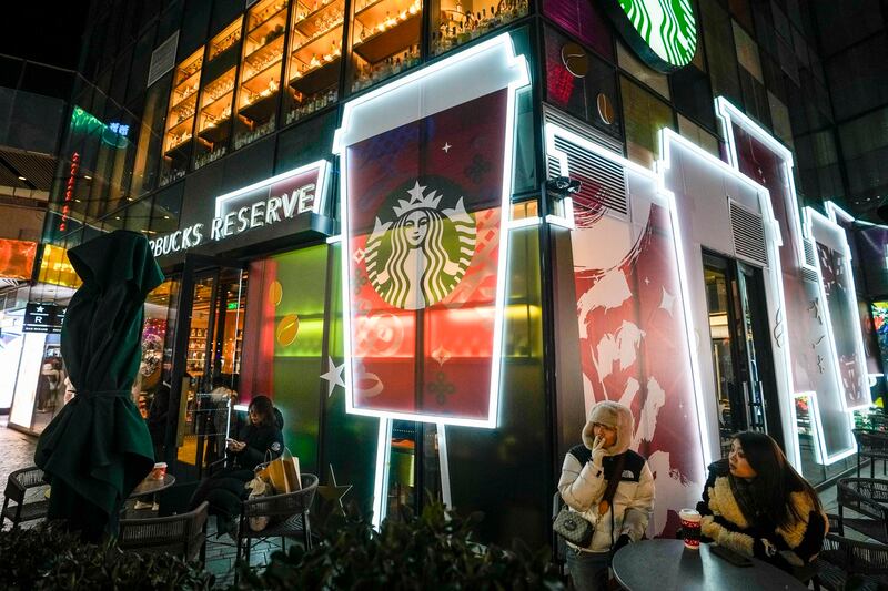 People drink coffee outside a Starbucks at a shopping mall in Beijing, Dec. 23, 2023. (Andy Wong/AP)