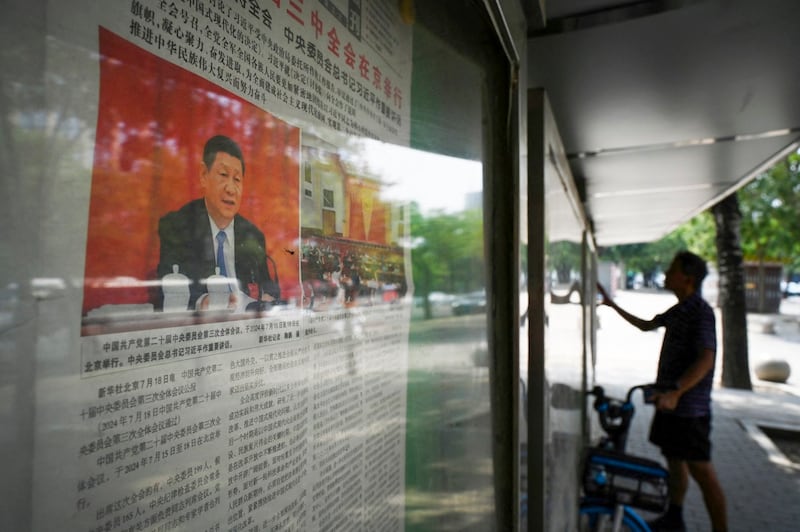 A man reads a newspaper near a front page photo of President Xi Jinping on a story about the conclusion of the Third Plenum, a key economic meeting, at a display board on a sidewalk in Beijing, July 19, 2024. (Greg Baker/AFP)