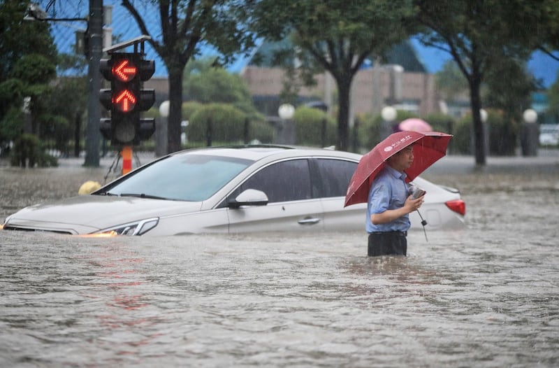 This photo taken on July 20, 2021 shows a man wading past a submerged car along a flooded street following heavy rains in Zhengzhou in China's central Henan province. (Photo by STR / AFP)