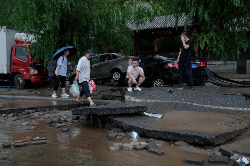 People walk along a damaged road and vehicles swept by flood water in the Mentougou District as continuous rainfall triggers alerts in Beijing, Monday, July 31, 2023. Credit: AP