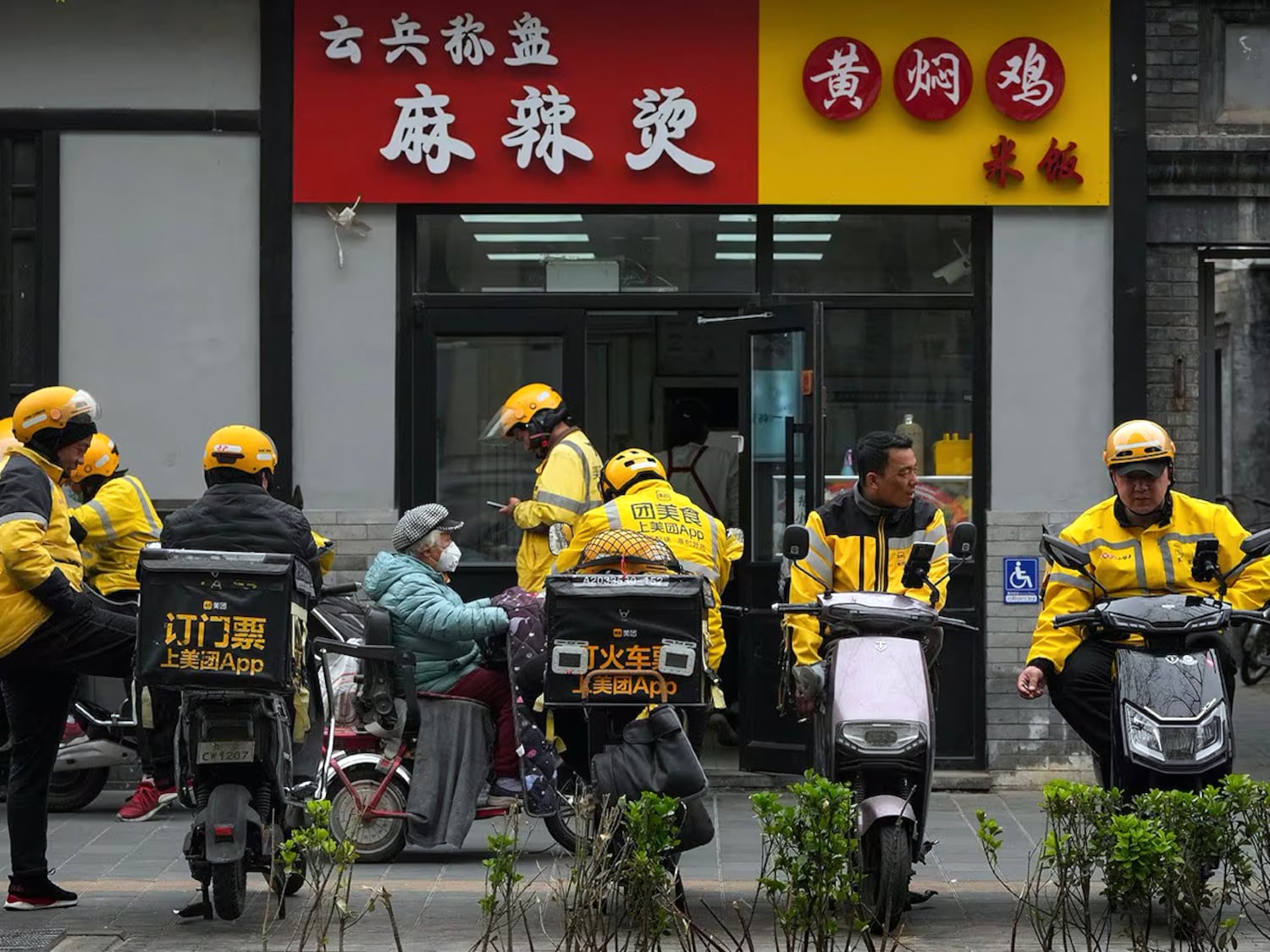 Food delivery workers wait for online orders outside a restaurant in Beijing, April 3, 2023.