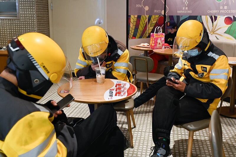 Food delivery riders wait in a restaurant at a shopping mall in Beijing on March 20, 2024.