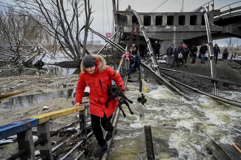 Civilians cross a river on a blown up bridge on Kyiv's northern front on March 1, 2022. Credit: AFP