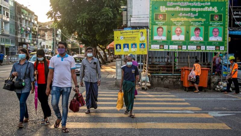 Pedestrians walk past election campaign posters as they cross a road in Myanmar's commercial hub Yangon, Oct. 7, 2020.