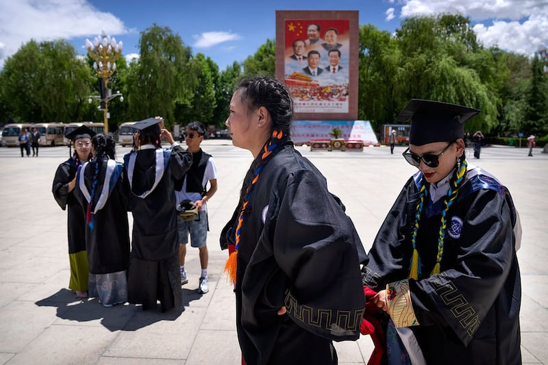 西藏大学理学院的毕业生们站在一张巨幅现任和前任中国领导人的照片前准备合影。（美联社）