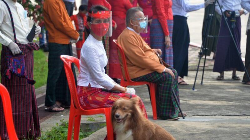 Aung San Suu Kyi (C), wearing a face mask and gloves to halt the spread of the coronavirus, waits with her dog to wave to supporters of her National League for Democracy party as they drive past in Naypyidaw, Sept. 19, 2020. AFP