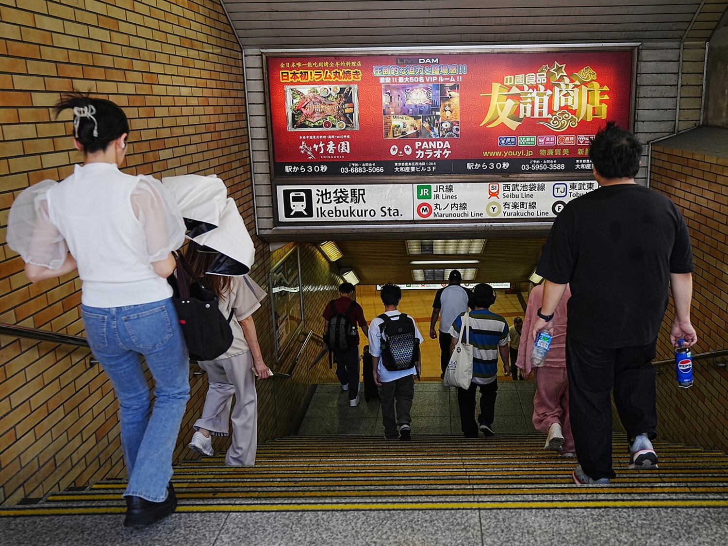 Die Pendler gehen an Werbung des chinesischen Restaurants und des Karaoke, die am 4. September 2024 in Tokio in Japan in Japan in Ikebukuro Station beliebt sind.