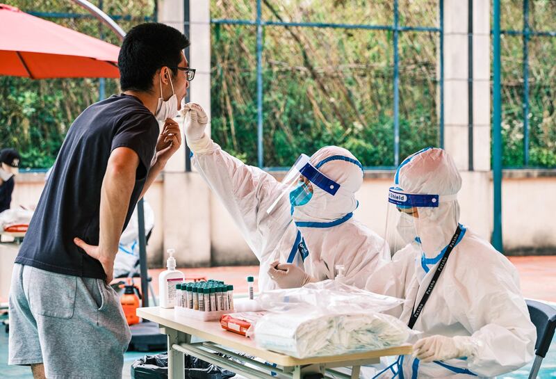 A health worker (C) wearing personal protective equipment conducts a swab test for the Covid-19 coronavirus in a compound during a Covid-19 lockdown in Pudong district in Shanghai on April 19, 2022. Credit: AFP