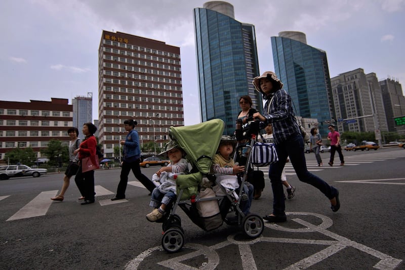 资料图片：北京商住区，一名中国妇女推着一辆载着两个孩子的手推车过马路 。（美联社）