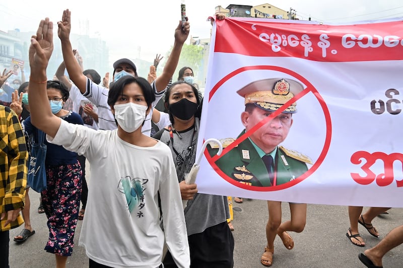 Protesters make the three-finger salute beside a banner featuring junta leader Min Aung Hlaing in a demonstration against the military junta in Yangon, July 3, 2021. Credit: AFP