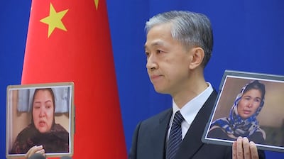 Chinese Foreign Ministry spokesman Wang Wenbin holds pictures of former internment camp detainees while speaking during a news conference in Beijing, Feb. 23, 2021, in this still image taken from video. Reuters