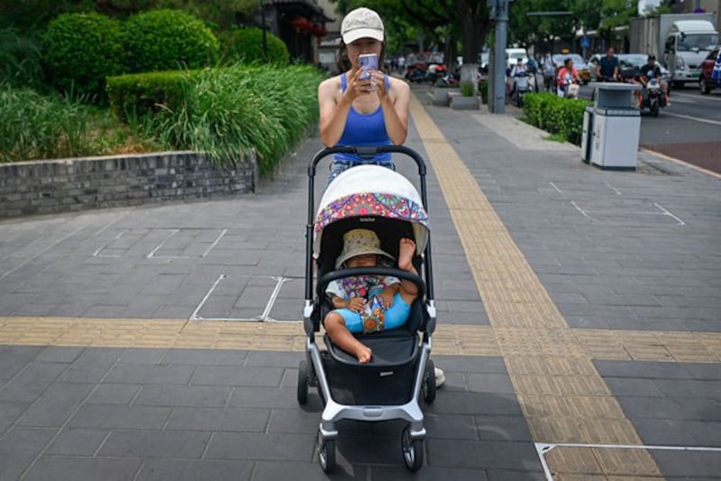 A woman pushing a baby carriage waits to cross a street in Beijing, July 10, 2023. (Wang Zhao/AFP)