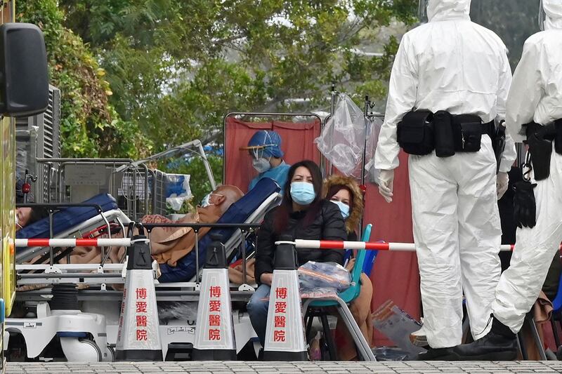 2022 年 2 月 15 日，随着确诊人数持续暴增，香港各大医院已难以负荷大批涌入的病患，香港博爱医院外的人们等待时，身穿防护装备的警察 (右) 在旁边站着。 （法新社）