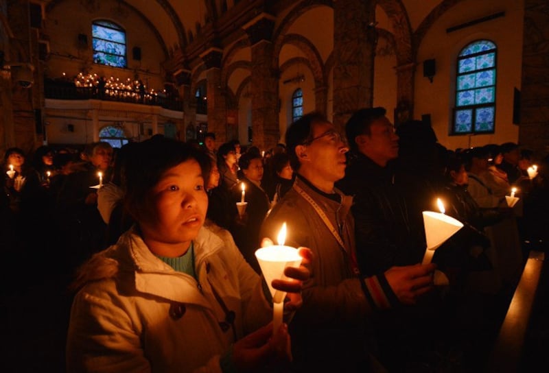 图片：2013年3月30日，在北京的一间教堂内，中国天主教徒们举蜡烛祈祷。（资料图片/法新社）