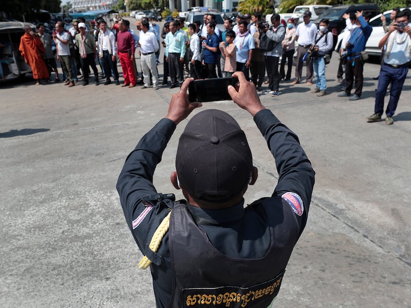 A Cambodia police officer takes photographs of opposition supporters while they wait during a hearing of their former National Rescue Party's President Kem Sokha at an appeals court in Phnom Penh, Cambodia, Jan. 30, 2024.