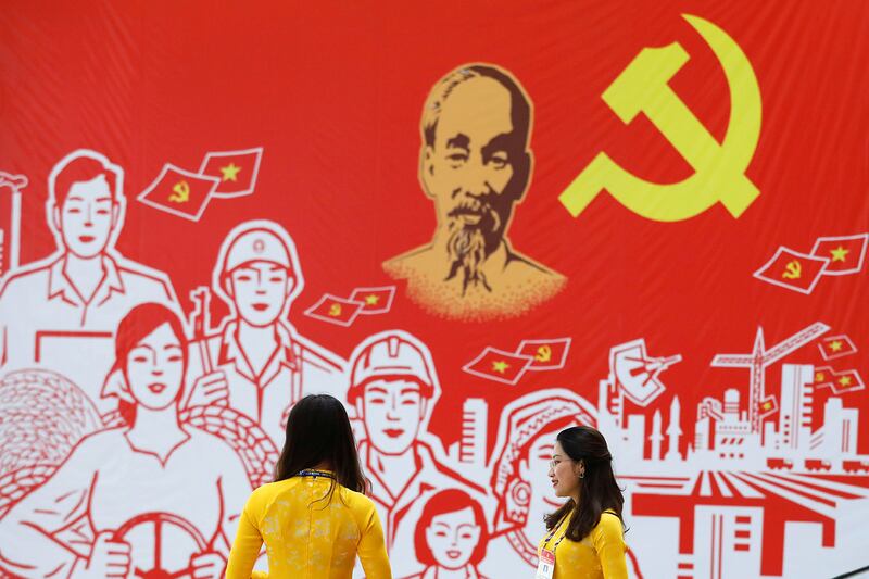 Women wearing traditional long dress 'ao dai', stand near a giant poster at the National Convention Center, the venue for the upcoming 13th national congress of the ruling Communist Party of Vietnam, in Hanoi, Vietnam January 22, 2021. REUTERS/Kham