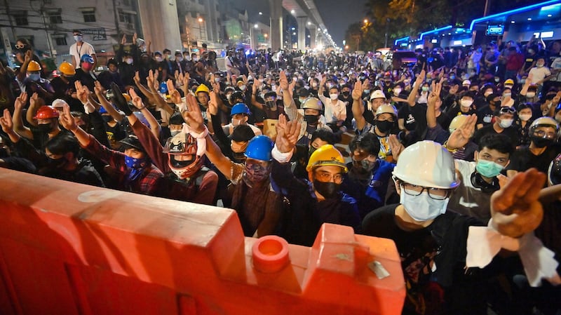 Pro-democracy protesters give the three-finger salute as they sit behind barricades during an anti-government rally at Kaset intersection in Bangkok, Oct. 19, 2020.