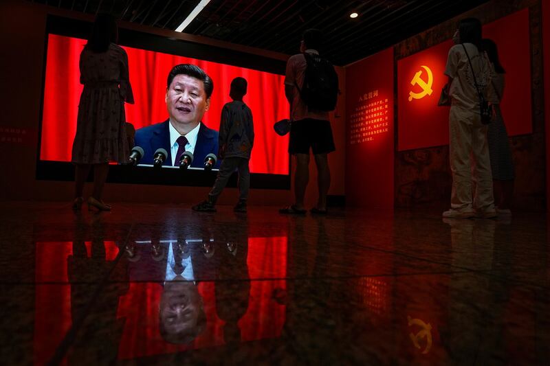 Visitors watch a screen displaying Chinese President Xi Jinping's speech next to a Communist Party's flag, at an exhibition promoting China's achievement under communist party from 1921 to 2021, in Beijing, June 20, 2021. Credit: Andy Wong/AP