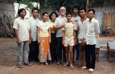 At a Thai camp, Father Robert Venet poses with Cambodian refugees in front of a church made from bamboo, 1986.