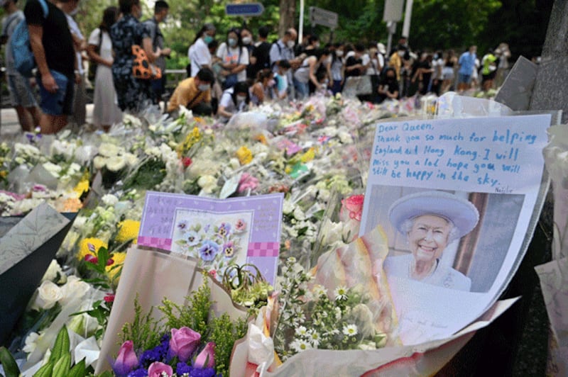 People gather next to flowers placed as a tribute outside the British Consulate in Hong Kong on Sept. 12, 2022, following the death of Britain's Queen Elizabeth II. Credit: AFP