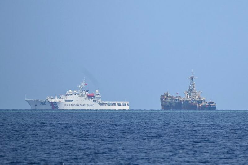 A Chinese coast guard ship (left) sails past the grounded Philippine navy ship where marines are stationed to assert Manila's territorial claims in the disputed South China Sea, Aug. 22, 2023. Credit: Ted Aljibe / AFP