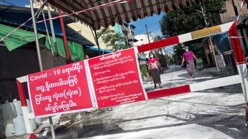 People walk towards a barrier blocking access to minor roads with a sign urging residents to stay at home due to a surge in the number of cases of the coronavirus in Myanmar's commercial city Yangon, Sept. 11, 2020. 