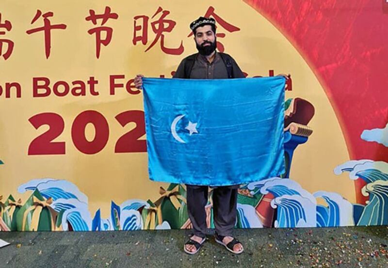 Pakistani student Muhammad Usman Asad holds the flag of East Turkistan, Uyghurs' preferred name for Xinjiang, in front of a billboard announcing a Dragon Boat Festival event at the National University of Sciences & Technology in Islamabad, Pakistan, June 10, 2022. Credit: Mumahhad Usman Asad