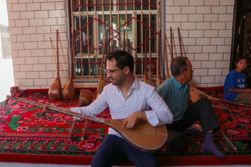 Hector Dorbecker, counselor for economic-commercial and financial affairs at the Embassy of Mexico in Beijing, tries to play dutar, a long-necked two-stringed lute, in Jiayi village of Xinhe county, northwest China's Xinjiang Uygur Autonomous Region, Aug. 2, 2023. Credit: Zhao Chenjie/Xinhua via Getty Images