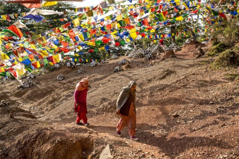 Women walk under strings of Tibetan prayer flags on a mountain path in Dharamshala, India, Feb. 10, 2023. (Ashwini Bhatia/AP)