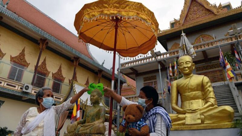 Cambodian women wearing face masks to protect themselves from the coronavirus pour water over a Buddha statue during the Khmer New Year at a pagoda in Cambodia's capital Phnom Penh, April 15, 2020.