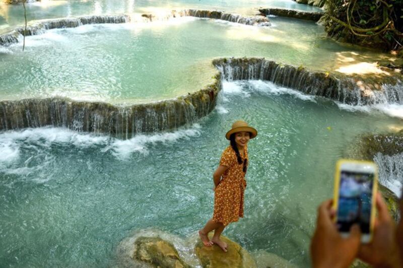 A tourist poses for photographs against the backdrop of the Kuang Si waterfalls, a popular tourist spot around 30 km (18 miles) outside of Luang Prabang, Laos, April 2019. Credit: AFP