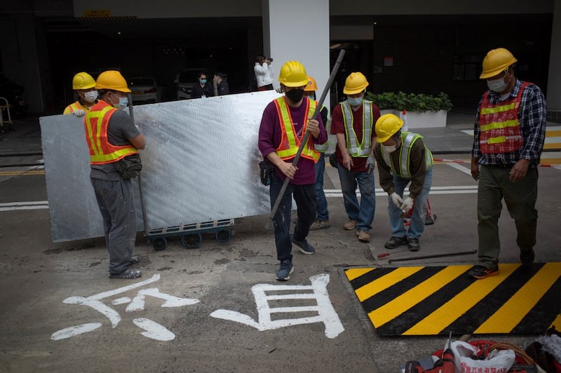 Construction workers stand next to Chinese characters reading "cold blood" on the ground as they use metal sheeting to cover up one of the last public tributes in Hong Kong to the deadly 1989 Tiananmen Square massacre which has adorned a campus footbridge at the University of Hong Kong (HKU) for over three decades, Jan. 29, 2022. Credit: AFP.