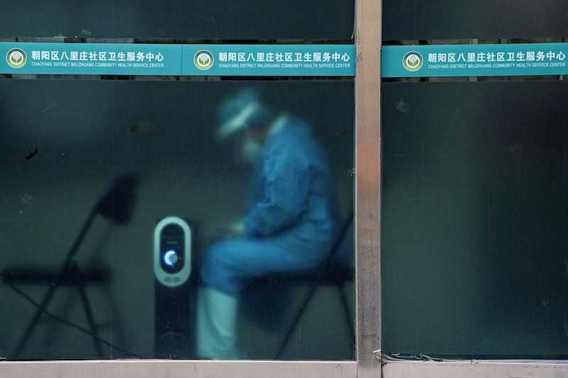 A worker in personal protective equipment keeps warm by a heater near a residential area under lockdown due to COVID-19 restrictions in Beijing, Nov. 29, 2022. Credit: Noel Celis/AFP