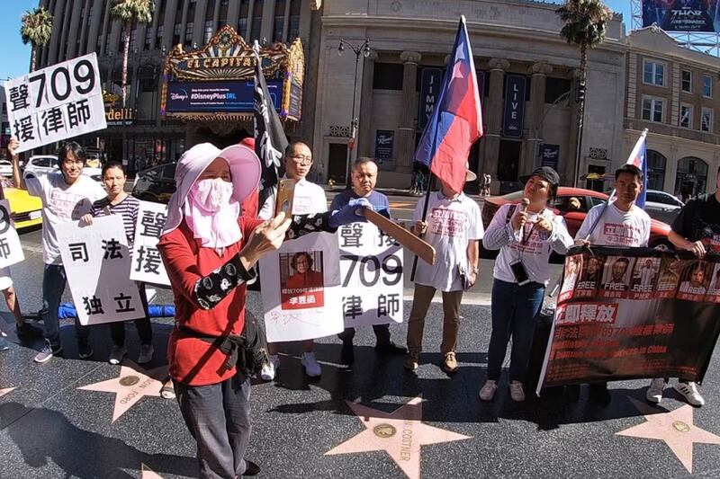 A woman who later threatened participants with a stick uses her phone to video a human rights protest by overseas China at the Hollywood Walk of Fame.