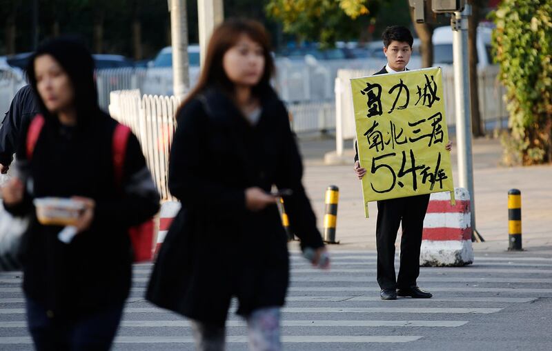 北京街道上，一名房地产经纪人（右）举着待售公寓的广告牌。（路透社）