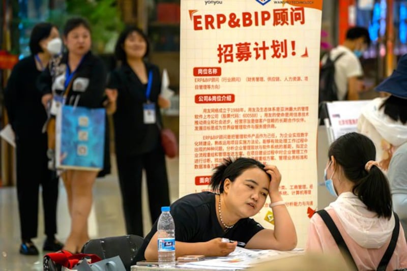 A recruiter talks with an applicant at a booth at a job fair at a shopping center in Beijing, China, on June 9, 2023. (Mark Schiefelbein/AP)