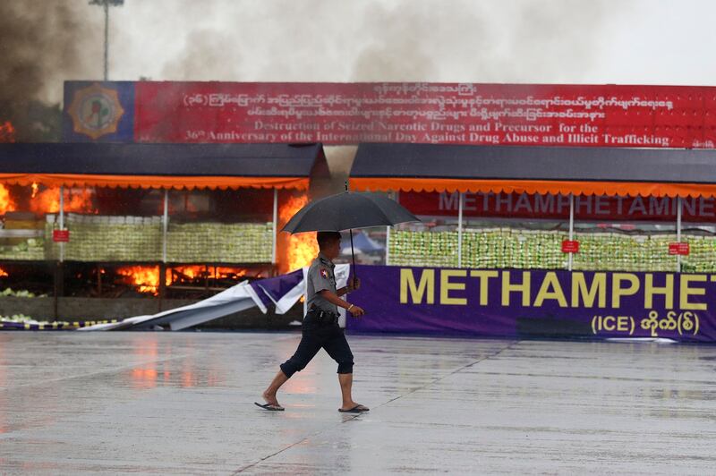 A police officer walks past burning illegal narcotics during a destruction ceremony marking the International Day against Drug Abuse and Illicit Trafficking on the outskirts of Yangon, Myanmar, Monday, June 26, 2023. Credit: Thein Zaw/Associated Press