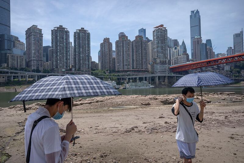 2022 年 8 月 19 日，学生们撑着雨伞站在重庆市嘉陵江干涸的河床上。(美联社)