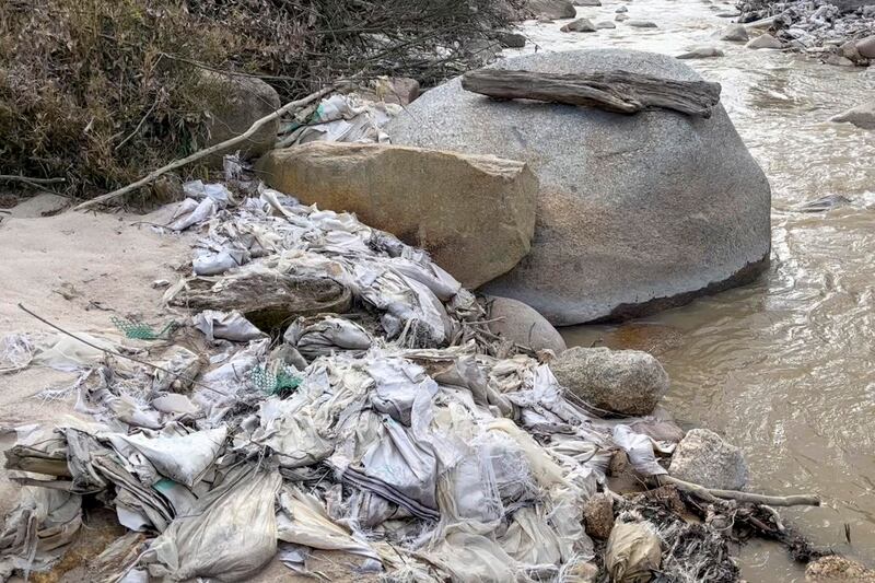 In this early 2022 image from video, a creek in Myanmar's Kachin state is lined with trash, pipes and other construction materials from a former rare earth mining site. Local villagers have said water from the creek is no longer usable for drinking or growing crops and that their skin itches after being exposed to water near rare earth mining sites. Credit: Global Witness via AP