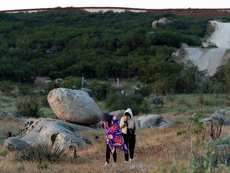 Chinese asylum seekers walk in Jacumba Hot Springs, Ca., away from the border wall with Mexico, background, to await processing by U.S authorities, May 8, 2024.