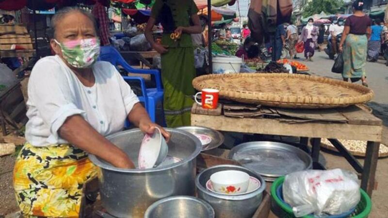 A Myanmar food vendor wearing a protective face mask washes dishes at a public market in the central Myanmar city of Mandalay, April 2020.