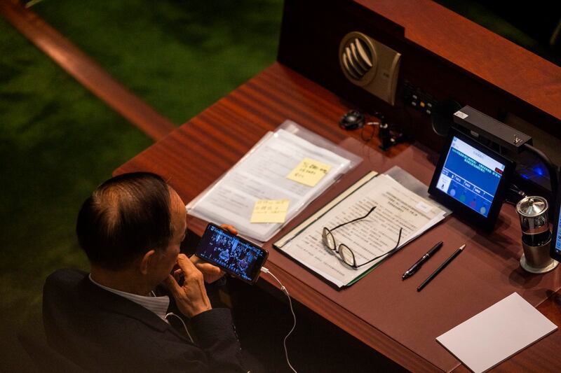 A pro-China lawmaker watches a video on a phone showing the 1945 Yalta Conference during the third reading of a bill that will overhaul district council elections in Hong Kong, July 6, 2023. Credit: Louise Delmotte/AP