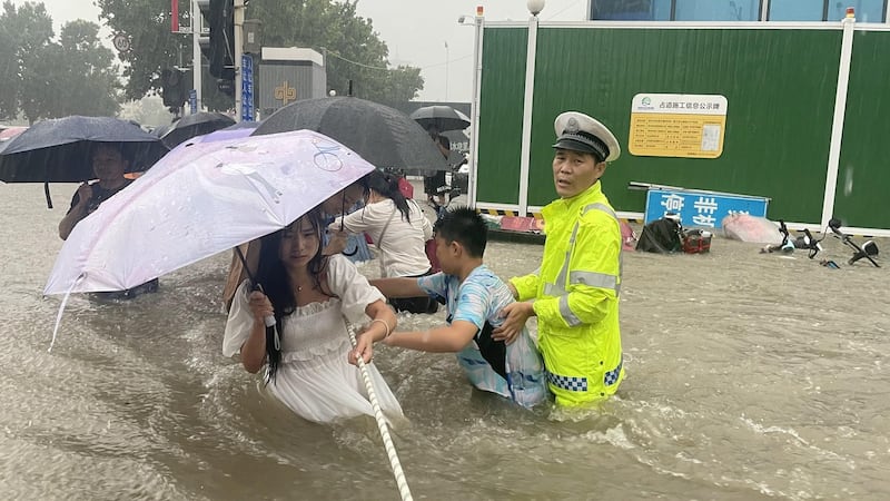 A traffic police officer guides residents to cross a flooded road with a rope during heavy rainfall in Zhengzhou, Henan province, China July 20, 2021. Picture taken July 20, 2021. China Daily via REUTERS