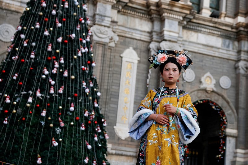 2024年12月20日，一名穿着旗人服装的女子，在北京市一所教堂的圣诞树前留影。