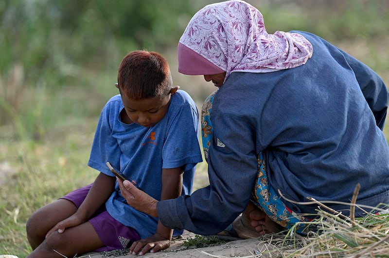 A woman and her son watch a video on a smartphone next to the Mekong River in Phnom Penh on Jan. 4, 2023. (Tang Chhin Sothy/AFP)