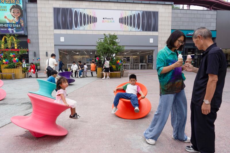 A woman shares ice-cream with a man as children play at a commercial complex in Beijing, July 15, 2024. (Ng Han Guan/AP)