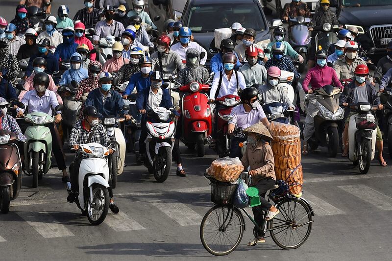 A bread vendor cycles past motorists waiting at a traffic light in Hanoi on June 2, 2021.