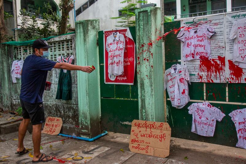 An anti-coup protester splashes red paint on student uniforms hung outside a school during a demonstration against the re-opening of the school by the junta in Yangon, April 27, 2021. Credit: AP Photo