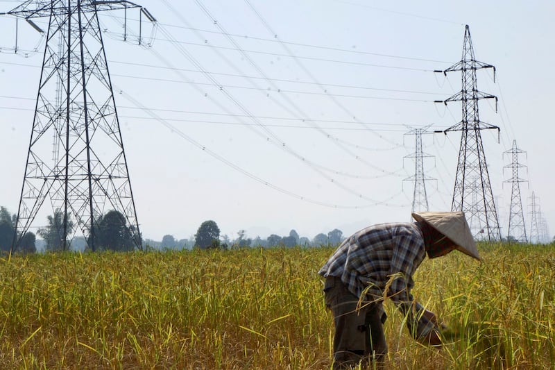 A farmer works in a paddy field under the power lines near Nam Theun 2 dam in Khammouane province in 2013. In September 2020, Laos state-owned energy company partnered with China Southern Power Grid Company to create the Électricité du Laos Transmission Company, of which China Southern has a controlling share and will manage Laos' power grid for the next 25 years. Credit: Aubrey Belford/Reuters