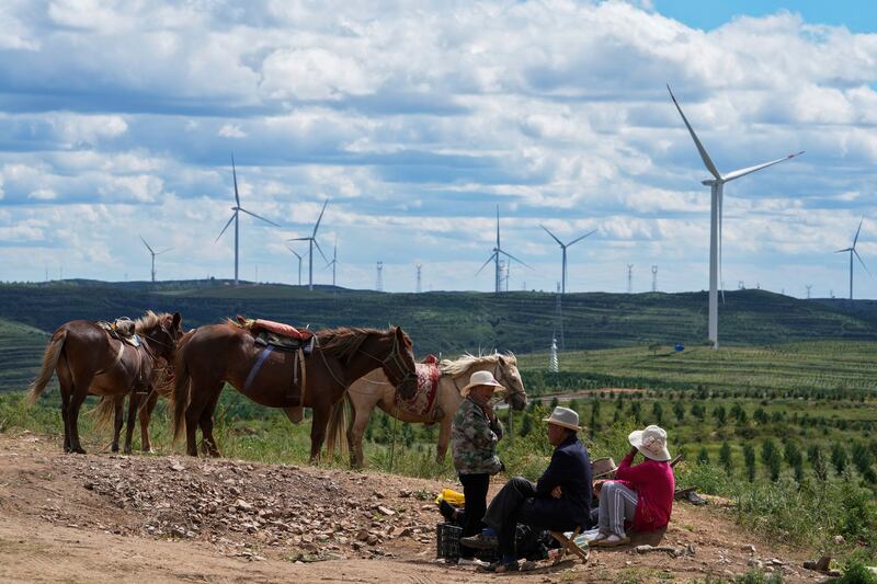 Villagers take a rest near horses on the grassland with wind turbines in the background in Zhangbei county, in north China's Hebei province, Aug. 15, 2022. Credit: AP